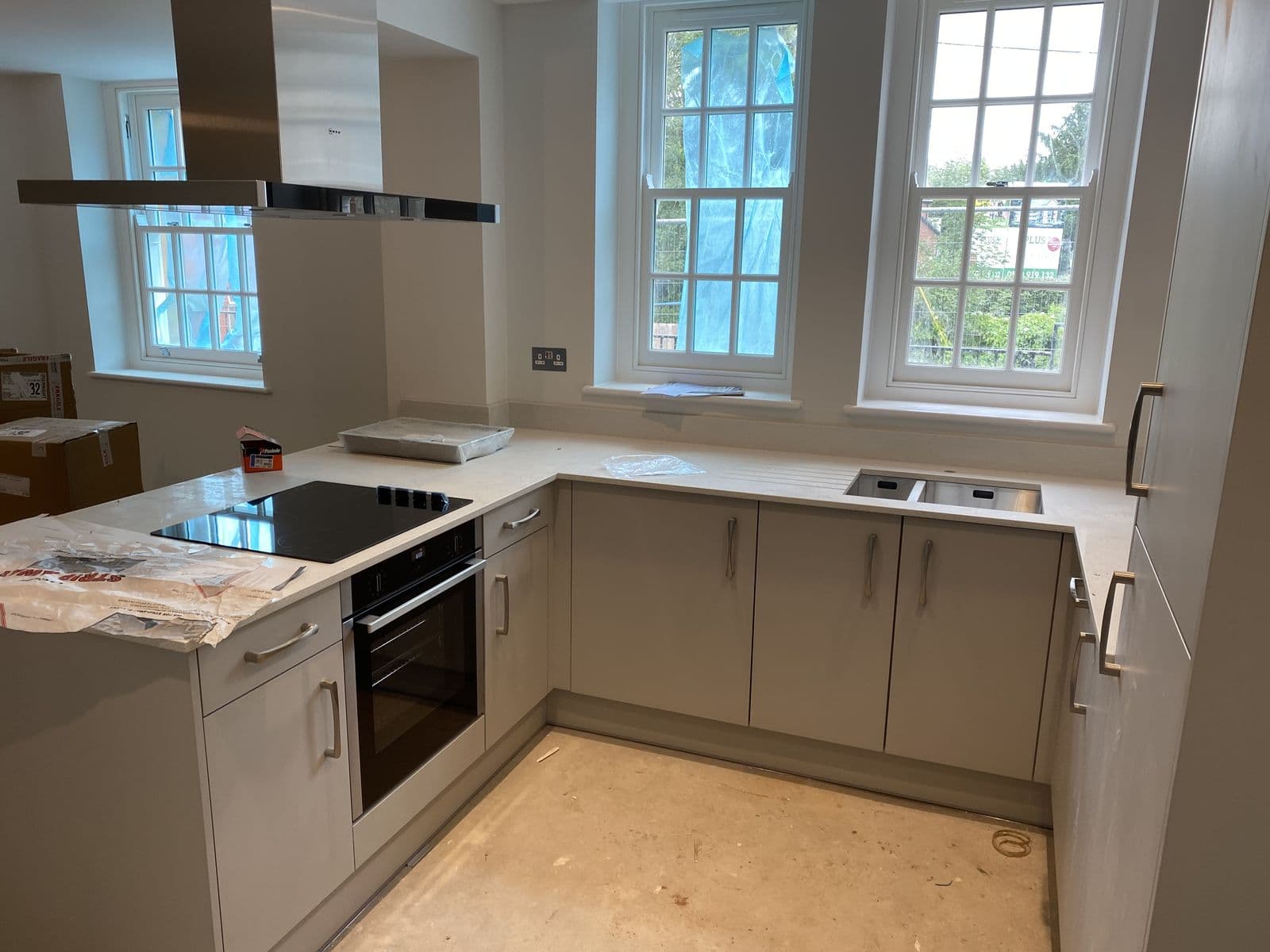 L-shaped grey kitchen with built-in oven beneath sash windows